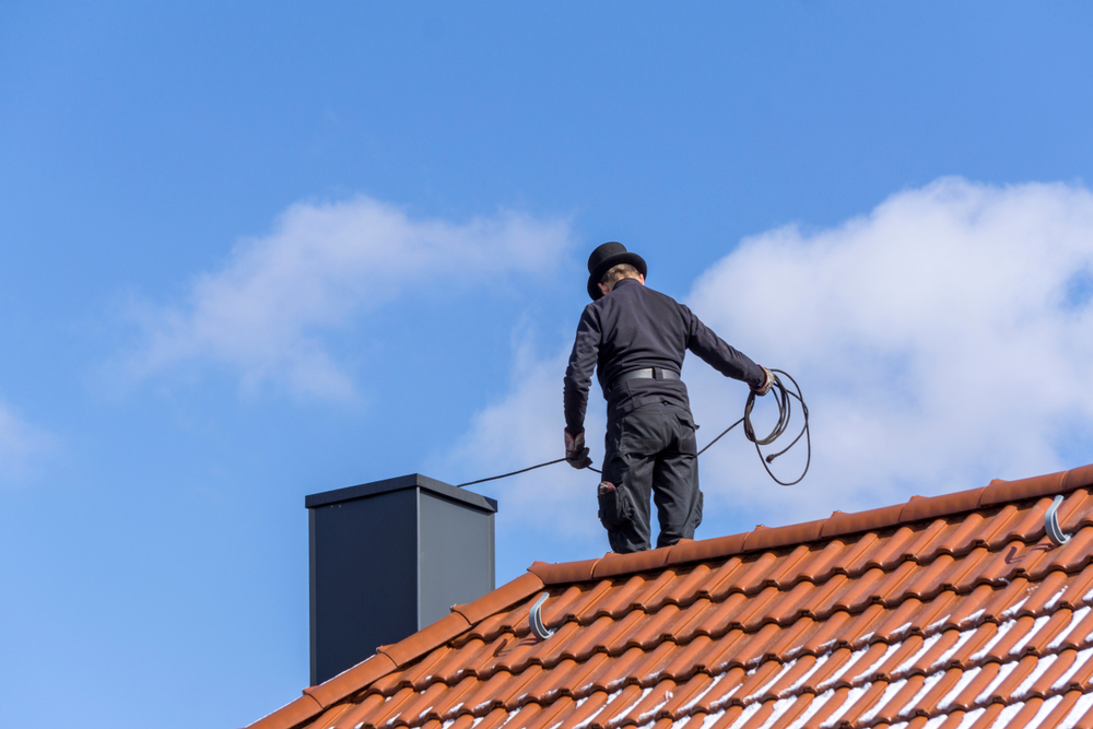 Chimney,sweep,cleaning,a,chimney,standing,on,the,house,roof,
